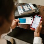 Pessoa realiza um pagamento online com um smartphone e um cartão de crédito em ambiente interno.