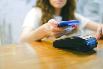 Mulher aproxima o smartphone de um terminal para realizar um pagamento por aproximação.