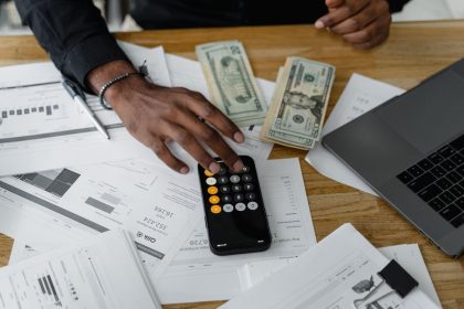 Documentos financeiros, calculadora, dinheiro e laptop organizados sobre uma mesa de trabalho.