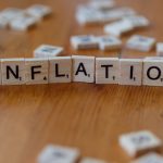 Peças de jogo de palavras formam a palavra “INFLATION” sobre uma mesa de madeira.