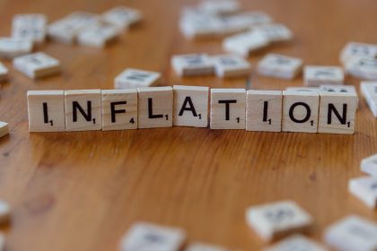 Peças de jogo de palavras formam a palavra “INFLATION” sobre uma mesa de madeira.