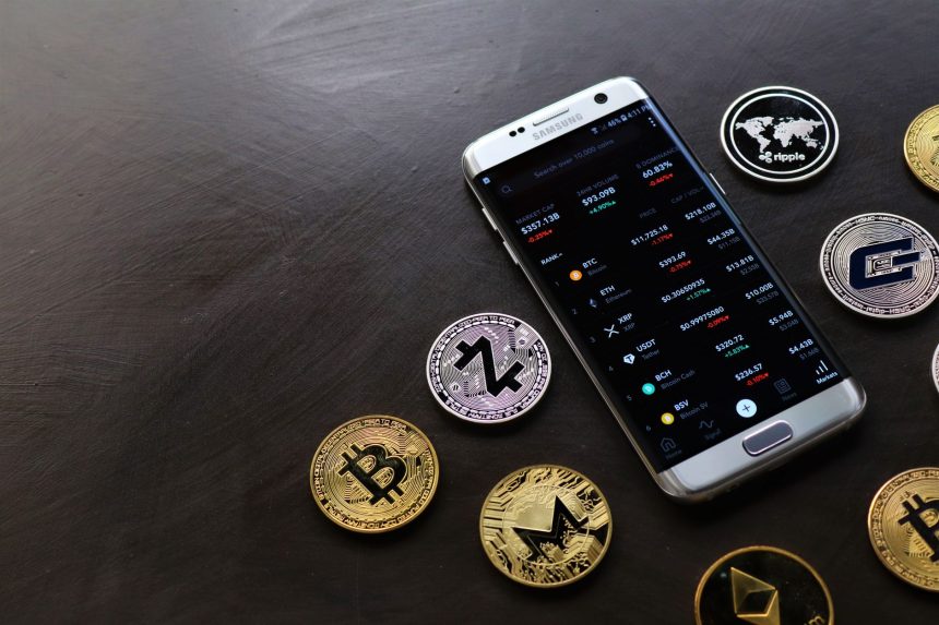 Moedas de criptomoeda ao lado de um smartphone que exibe uma plataforma digital de negociação.
