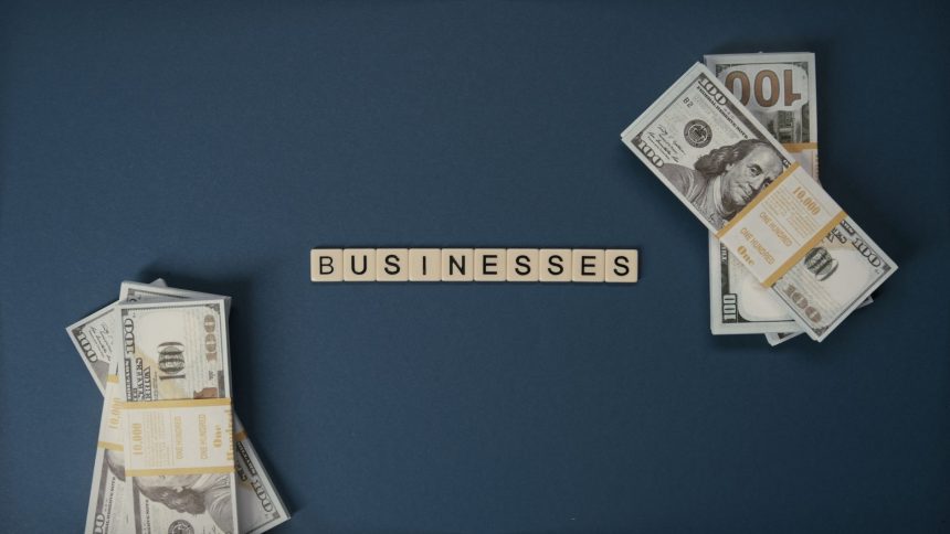 Cédulas de dólar dispostas ao lado de peças com a palavra “businesses”, em referência a negócios e transações financeiras.